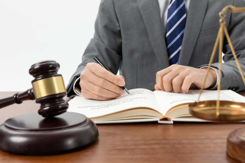 Person Writing on a Book with a Gavel on the Table